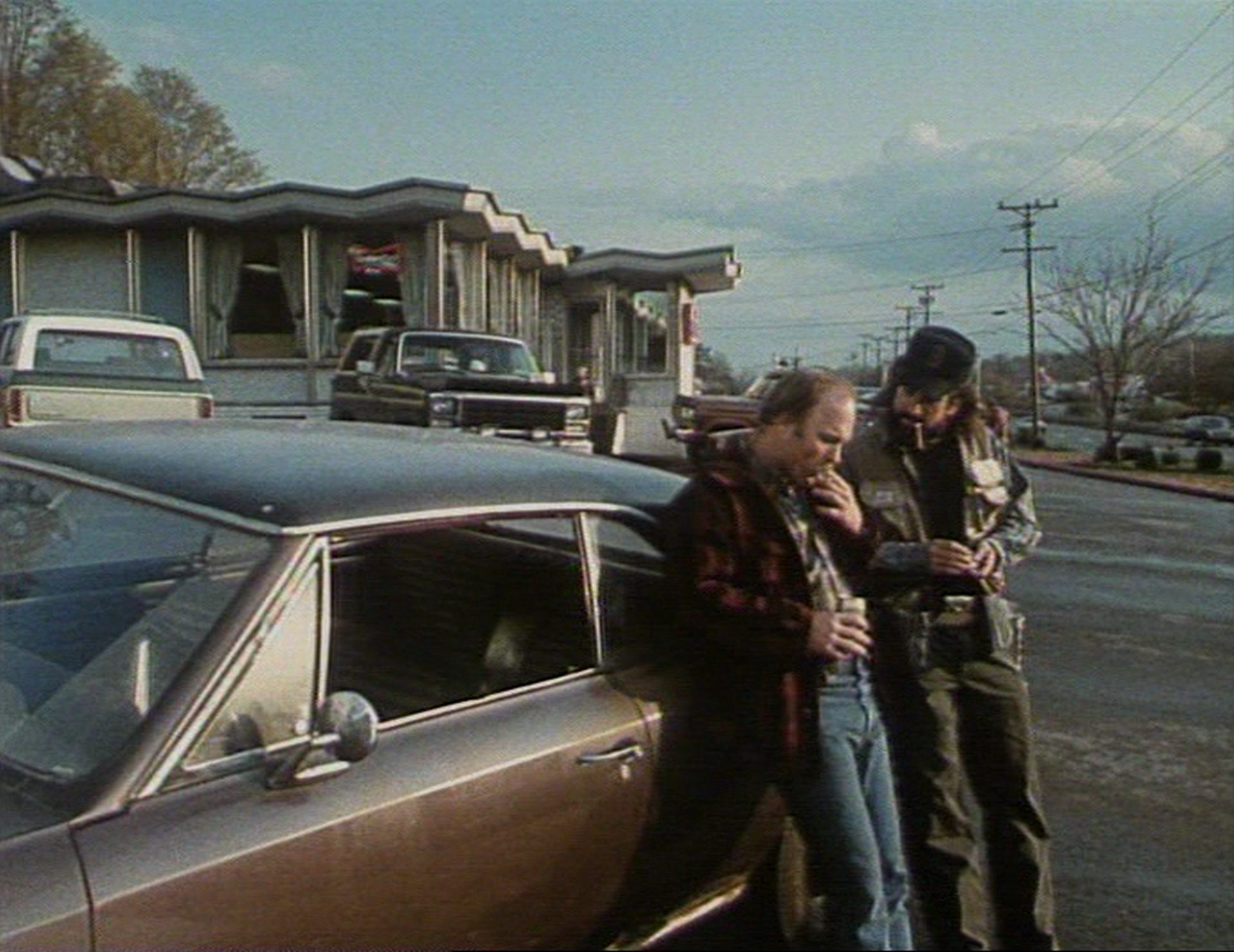 Ed Harris und Robert De Niro lehnen in proletarischem Look an einem Muscle car in trist-kleinstädtischer Umgebung.