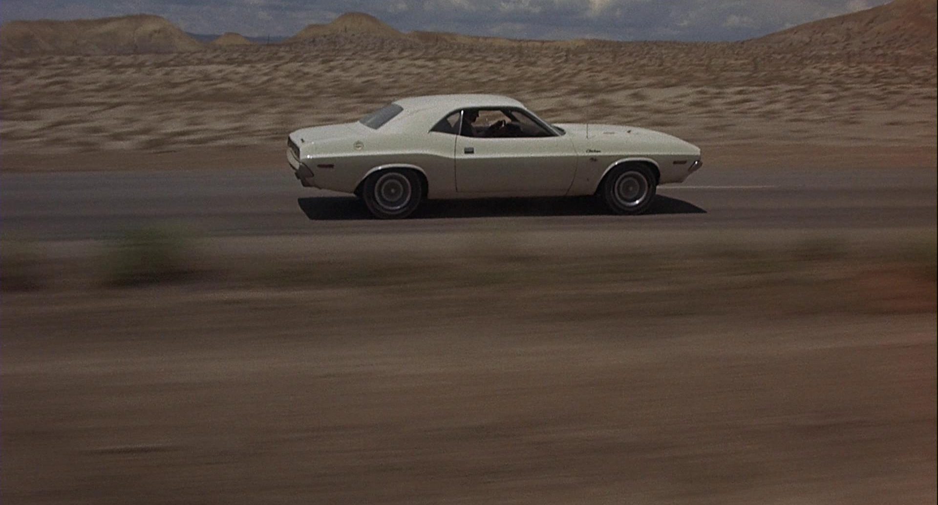 Der weiße Dodge bei schneller Fahrt durch eine karge Wüstengegend.