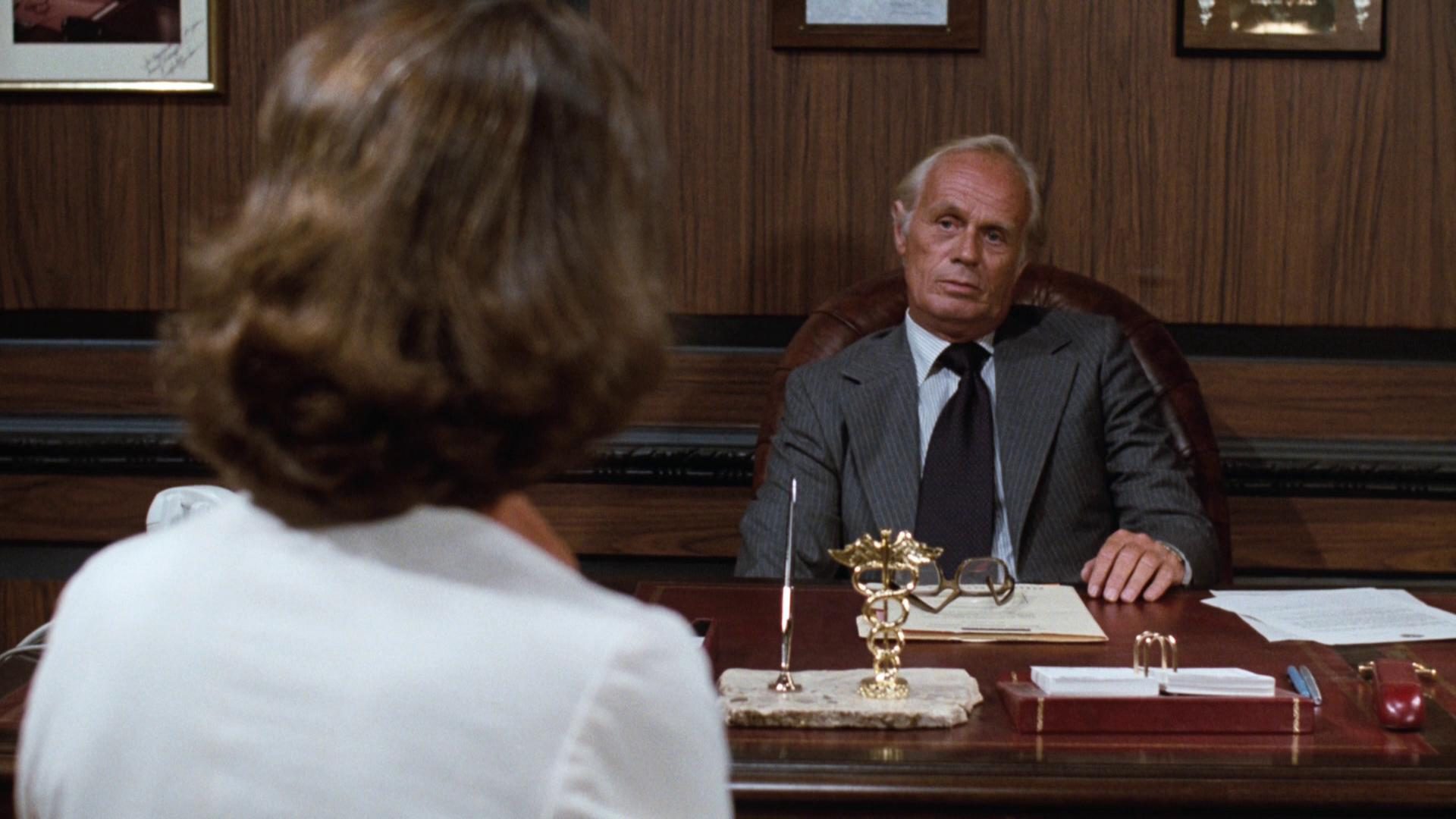 Richard Widmark als Chefarzt mit stoischer Miene an seinem Schreibtisch, Wheeler sitzt ihm mit dem Rücken zur Kamera gegenüber.