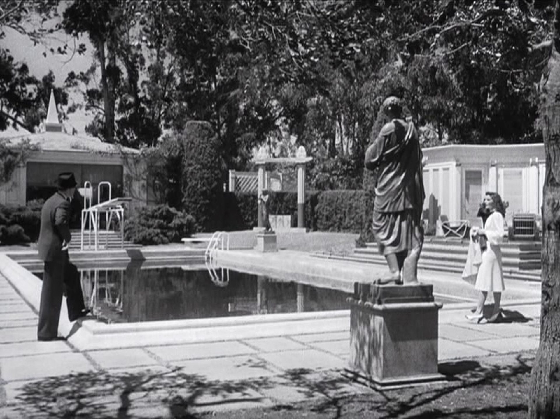 Blick auf den neoklassischen Swimmingpool des luxuriösen Anwesens, links und rechts stehen sich James Stewart und Katharine Hepburn gegenüber.