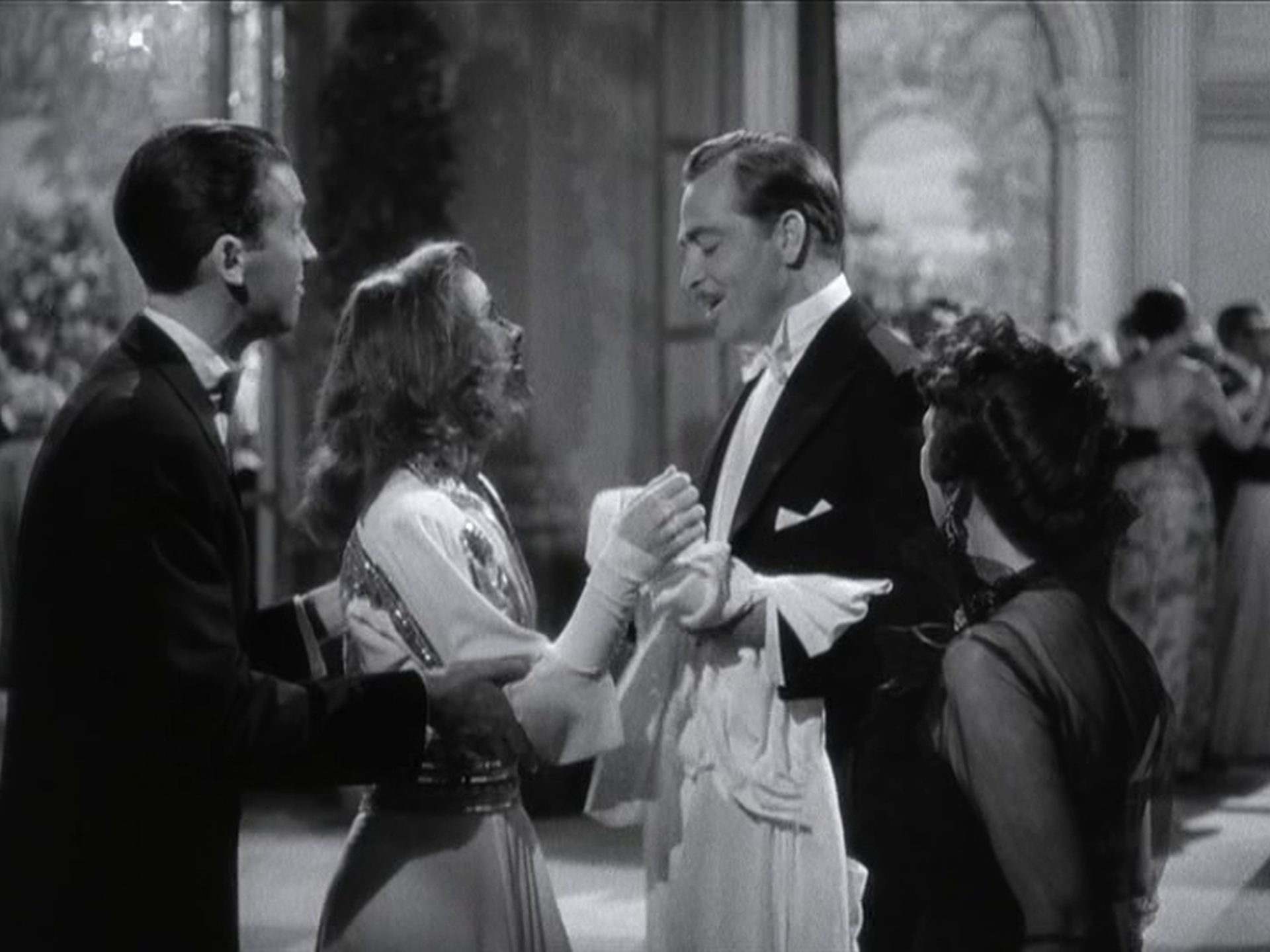 John Howard als George Kittredge im Beisein seiner Verlobten Tracy und dem Reporter Connor in einer Halle mit großbürgerlichem Flair.