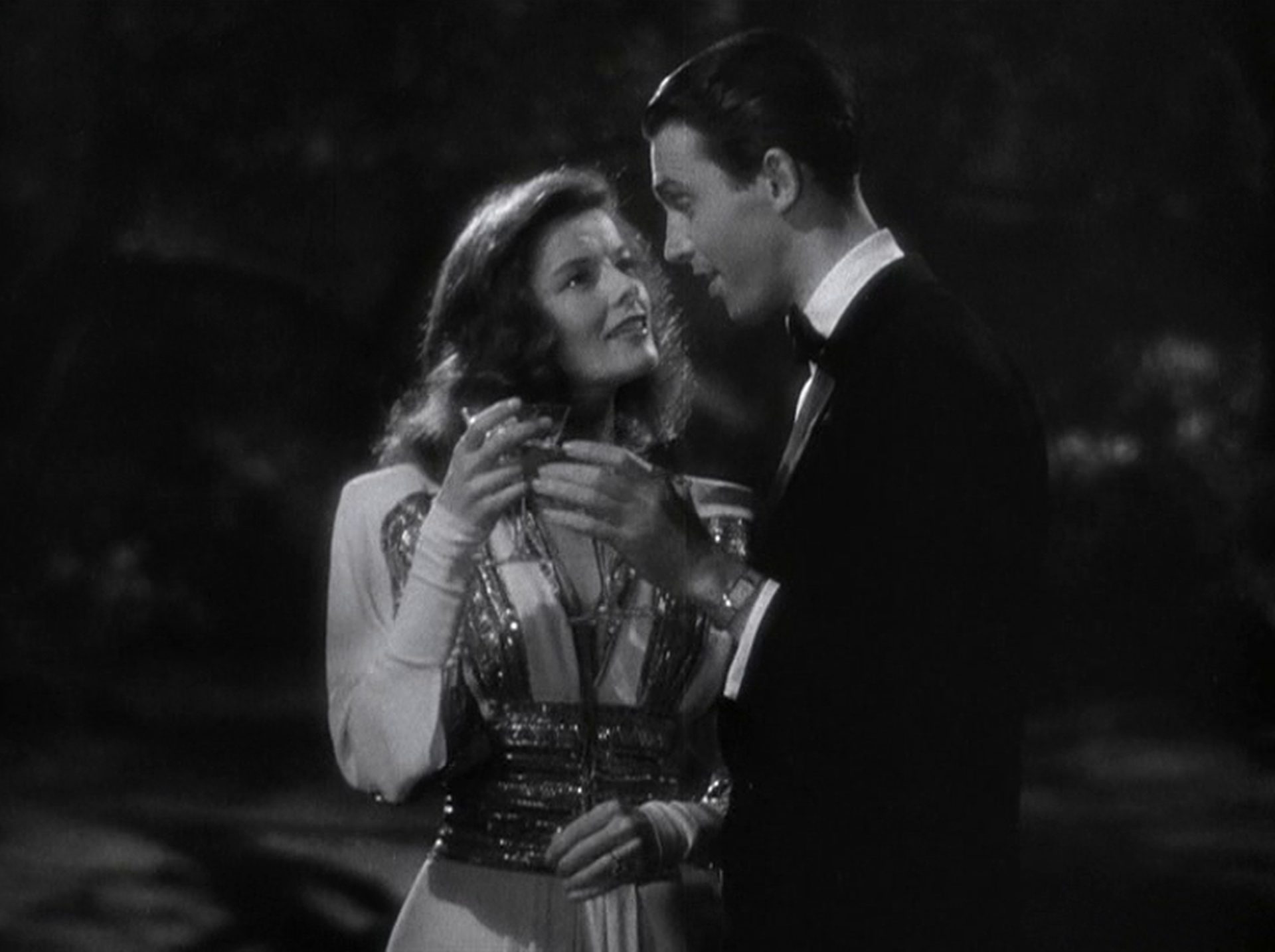 Katharine Hepburn als Tracy und James Stewart als Connor nachts in romantischer Nähe mit Drinks in der Hand.