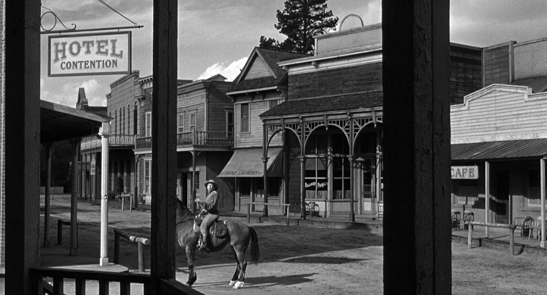 Mann zu Pferd alleine auf der Hauptstraße einer menschenleeren Kleinstadt; im Vordergrund ein Schlild mit der Aufschrift: Hotel Contention.