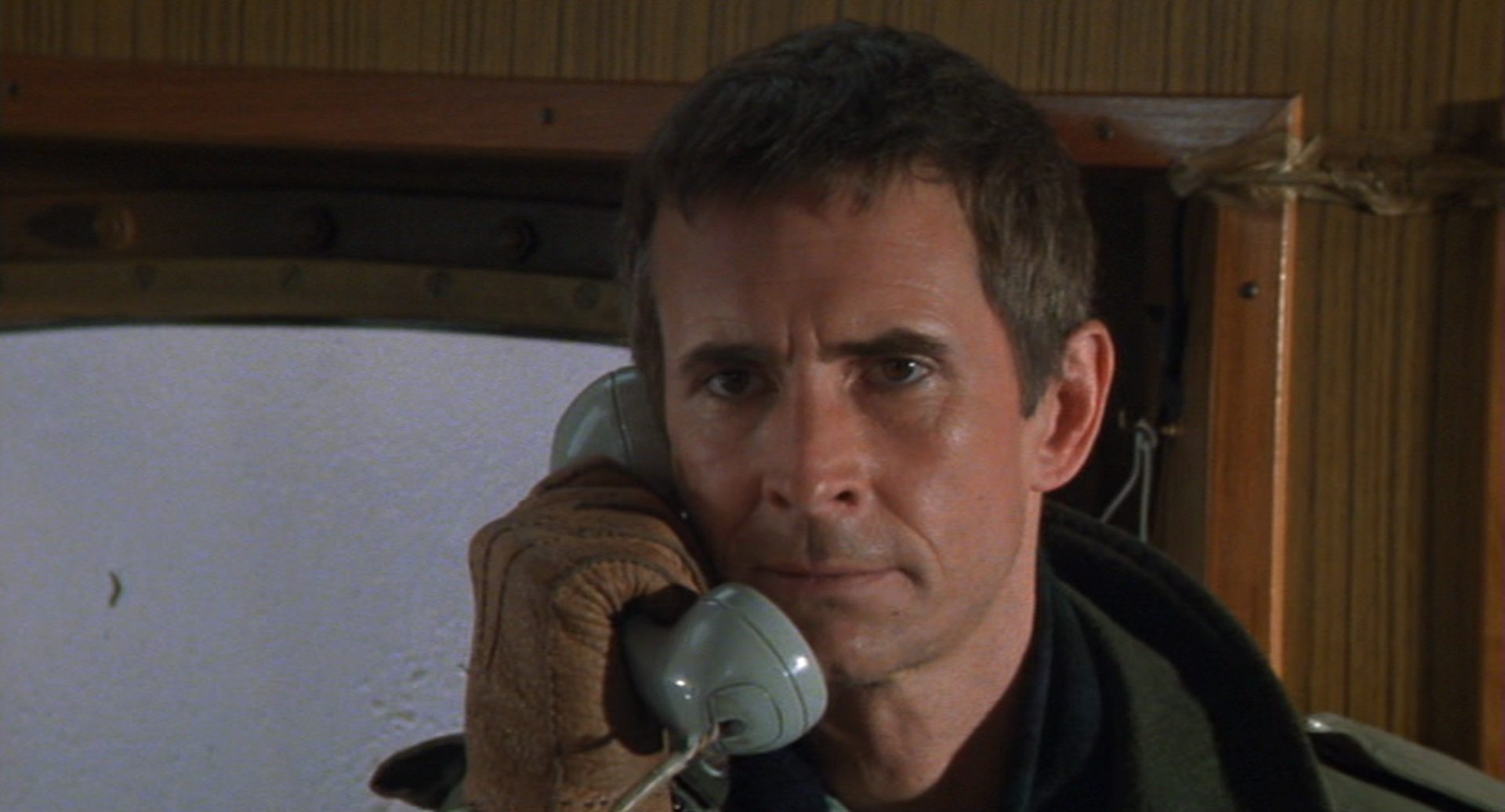 Nahaufnahme von Perkins als Kramer mit ernstem Gesichtsausdruck und dem Telefonhörer am Ohr.