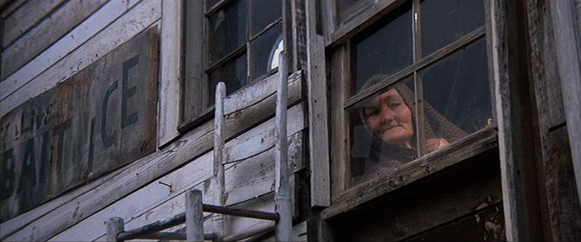 Eine alte Frau blickt aus dem Fenster eines alten Gebäudes aus Holzbrettern.