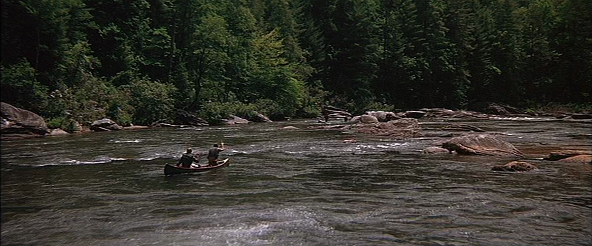 Blick aus der Distanz auf zwei Männer im Kanu im reißenden Fluss.
